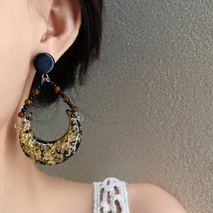 Détail de boucles d'oreilles lune en résine et feuille d'or avec perles
