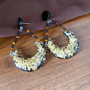 Détail de boucles d'oreilles lune rétro en résine noire avec des éclats de feuilles d'or
