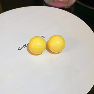 Close-up shot of bright yellow glossy round stud earrings on a white minimalist display