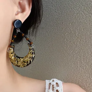Détail en gros plan de boucles d'oreilles vintage en résine dorée portées sur l'oreille