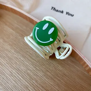Detailed shot of cream hair claw clip with a green smiley face charm
