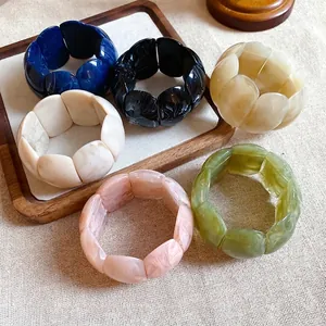 Stylish chunky marbled acrylic square bracelets in assorted colors on wooden tray.
