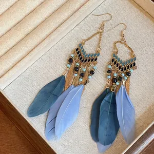 Detail of Bohemian style long drop earrings featuring blue feathers and golden beads