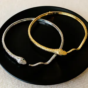 Macro view of gold and silver snake necklaces with intricate scale texture and green eyes
