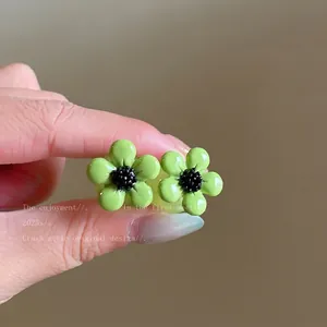 Detail view of green flower resin stud earrings with black center in forest style