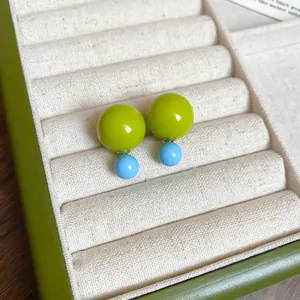 Close-up detail view of vibrant green and blue resin double-sphere stud earrings in tray