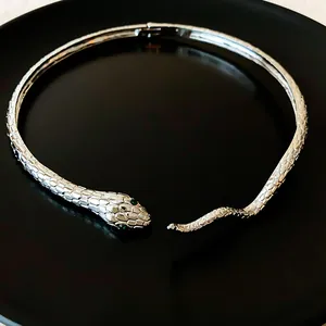 Macro view of silver snake-shaped choker with green gemstone eyes and detailed scales.