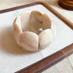 Macro view of a chunky cream marbled acrylic stretch bracelet on white linen background