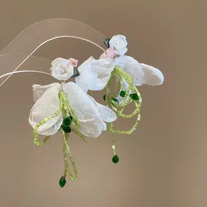 Detailed close-up of forest style white resin flower earrings with green beaded tassels
