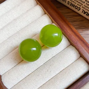 Close-up of vibrant green round resin stud earrings in a wooden jewelry tray