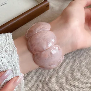 Detailed view of a chunky marbled acrylic bracelet in soft pink tones on a woman's wrist