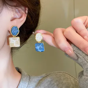 Vista detallada de pendientes irregulares azules y crema con diseño ondulado y oro chic