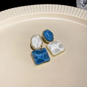 Vista detallada de pendientes geométricos irregulares con textura brillante azul y blanca