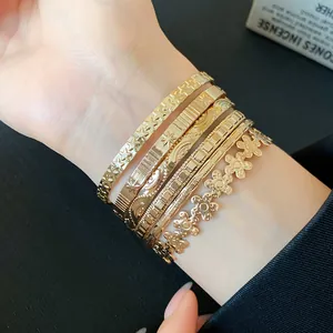 Detail shot of stacked gold bracelets featuring star and flower patterns on wrist.