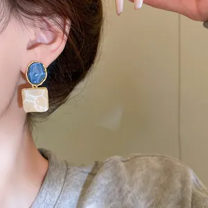 Primer plano de elegantes pendientes cuadrados irregulares con patrón de ondas de agua