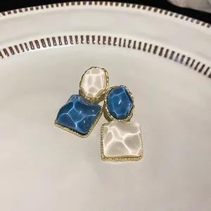 Detalle de pendientes geométricos con textura ondulada azul y blanca brillante
