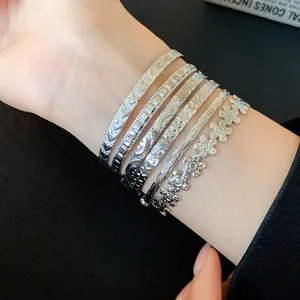 Detailed view of layered silver open bangles featuring floral, star and textured metal patterns