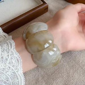 Detailed view of a wide amber marbled acrylic bangle worn on a wrist with lace detail.