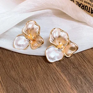 Macro detail of French retro three-petal flower stud earrings with a gold and pearlescent finish