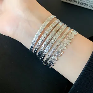 Detailed view of silver metal open bangles featuring flower and star patterns on a wrist