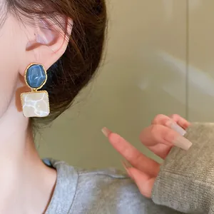 Primer plano de pendientes cuadrados irregulares con elegante acabado azul y perlado