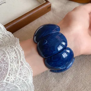 Detail view of a chunky dark blue marbled acrylic bracelet worn on a wrist with lace