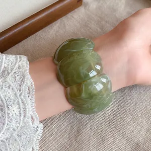 Detailed close-up view of a chunky green marbled acrylic bracelet worn on a lace-sleeved wrist.