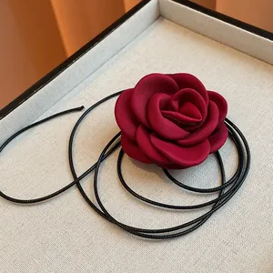 Detailed close-up of a deep red fabric rose necklace with a black woven leather cord