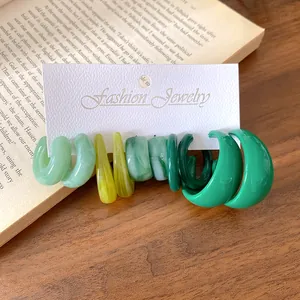 Primo piano di orecchini a cerchio a C in acrilico verde e giallo su cartoncino.