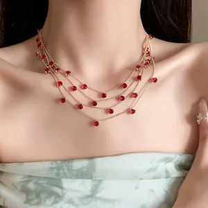 Détail du collier multi-rangs en chaîne dorée avec zircons rouges sur modèle