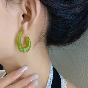 Primo piano di un orecchino a cerchio in acrilico verde a forma di C indossato da un modello