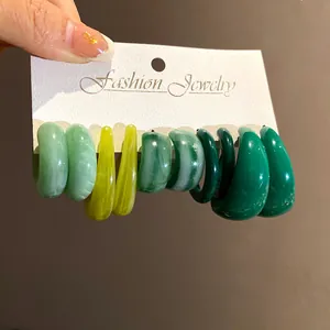 Dettaglio di un set di cinque orecchini a perno in acrilico verde a forma di C su carta
