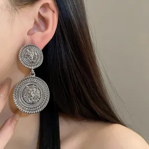 Close-up of silver-colored round drop earrings featuring an embossed lion head design.