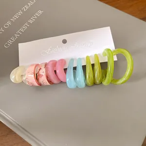 Dettaglio di orecchini a cerchio in acrilico colorato su cartoncino bianco.