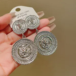 Detailed view of silver lion head earrings with textured circular drops