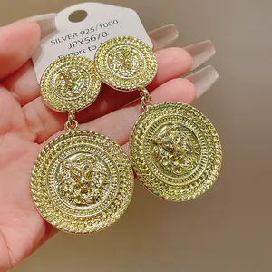 Close-up of golden circular earrings featuring intricate lion head relief design.