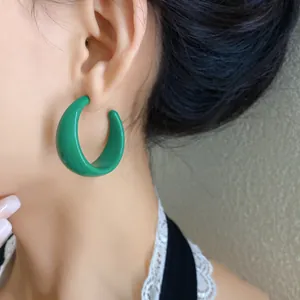 Primo piano di orecchini a cerchio a forma di C in acrilico verde brillante sul lobo