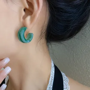 Primo piano di un elegante orecchino a cerchio a forma di C in acrilico verde sul modello