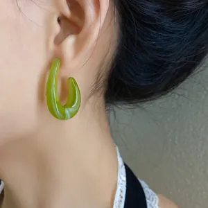 Primo piano di un orecchino a cerchio a C in acrilico verde con elegante motivo marmo.