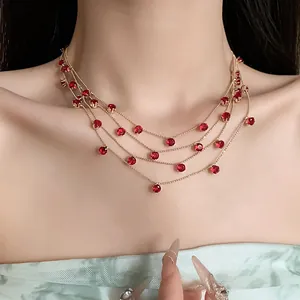 Vue détaillée d'un collier doré multicouche élégant avec des zircons rouges étincelants.