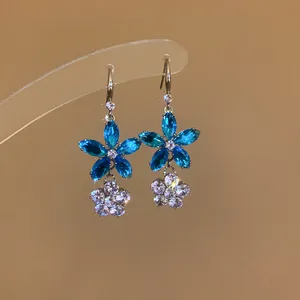 Nahaufnahme von eleganten blauen und klaren Zirkonia-Blumenohrringen mit Silberhaken