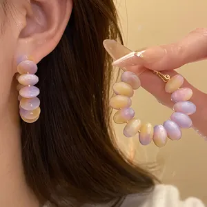 Detail of resin hoop earrings with purple and yellow gradient beads on silver needles.