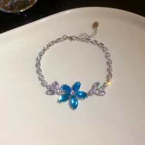 Makroaufnahme eines Armbands mit blauen Zirkonia-Blumen auf einer weißen Schale