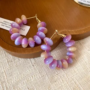 Detailed view of purple and peach resin bead hoop earrings with golden silver needles