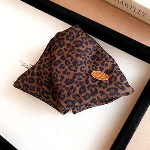 Close-up of a stylish triangle leopard print fabric hair clip with a gold metal badge