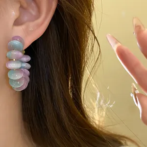 Close-up detail of gradient pastel resin disc hoop earrings worn on a model's ear.