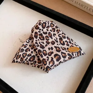 Close-up of a stylish leopard print fabric triangular hair clip with gold logo detail
