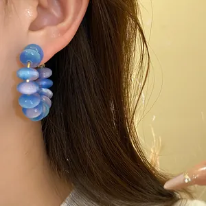Close-up detail of stylish blue and purple resin bead hoop earrings worn on ear