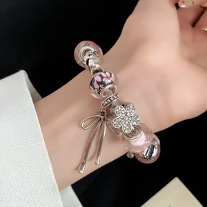 Close-up of a sweet pink glass bead charm bracelet with flower and bow pendants.