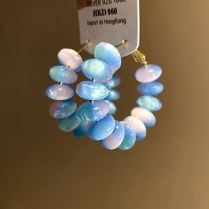 Close-up of blue resin hoop earrings with opalescent beads on a white display card.